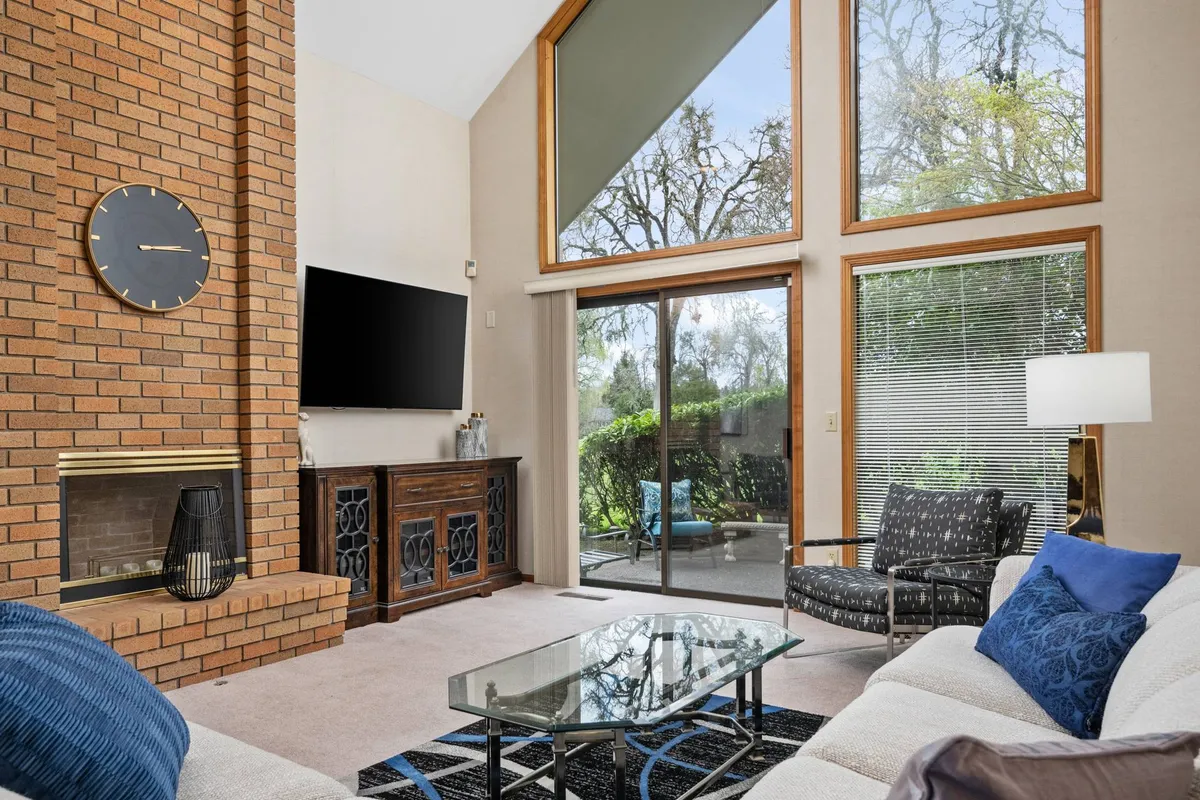 This interior image shows a spacious family room with a brick fireplace, large windows letting in plenty of natural light, comfortable seating, and a glass coffee table. The scene exudes warmth and offers a glimpse of the outside, suggesting a cozy spot to relax with pets after exploring the city.