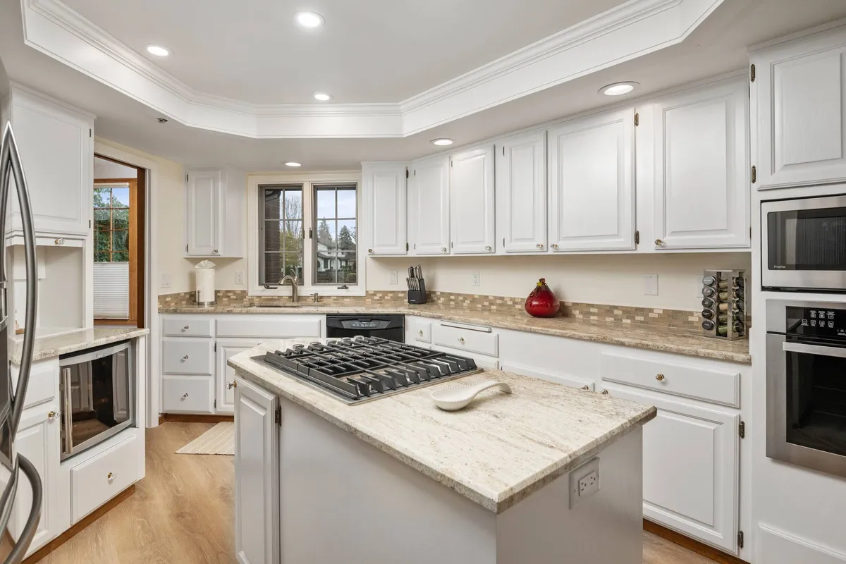 A contemporary remodeled kitchen with a central island, stainless steel appliances, white cabinetry, and a window providing a bright, welcoming atmosphere. The space is ideal for cooking, baking, and informal gatherings around the island.