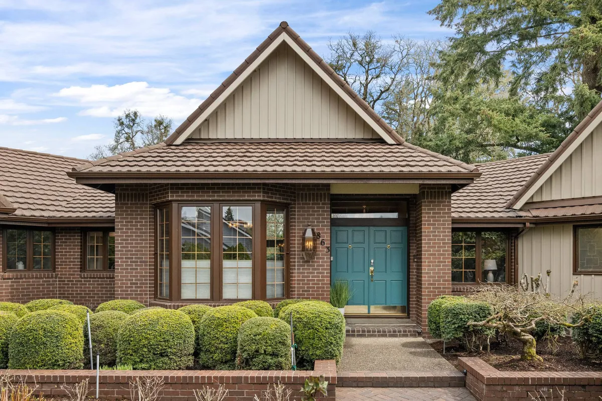 This exterior image captures the inviting front door of Fairway View Retreat surrounded by landscaped bushes and a brick facade. The well-maintained yard suggests open space for walks and outdoor gatherings, reflecting the home’s welcoming atmosphere for families and their pets.