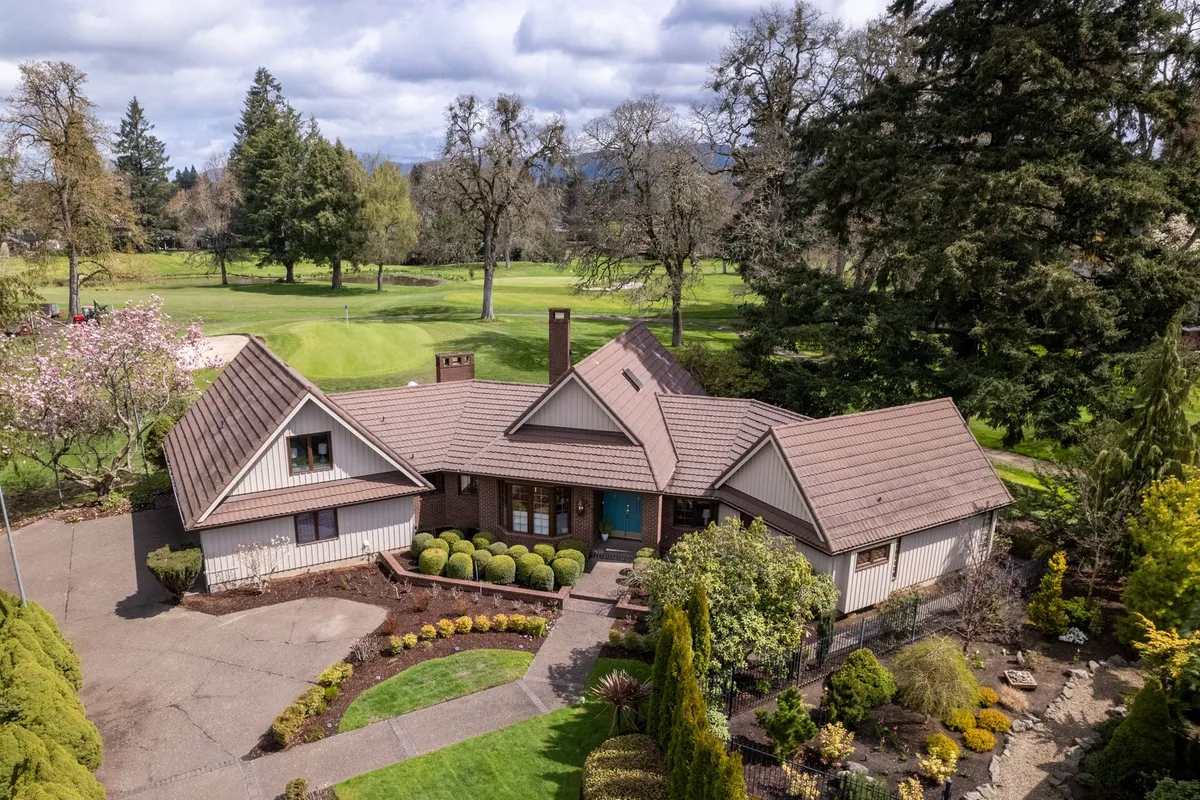 The hero image showcases a stunning, spacious single-family home set against lush, manicured gardens with vibrant flowers, all overlooking the rolling fairways of Oakway Golf Course. The scene is bathed in warm sunlight, with inviting outdoor seating hinting at relaxing afternoons, and the golf course visible just beyond the property line. The upscale neighborhood and tranquility of the cul-de-sac are evident, creating a serene, exclusive atmosphere.