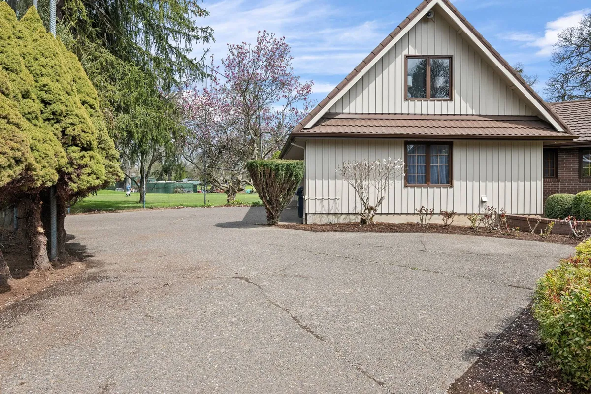 This image captures the house facade, framed by a driveway, mature trees, and a flowering tree in the foreground. The scene is inviting and hints at peaceful outdoor living and neighborhood charm.