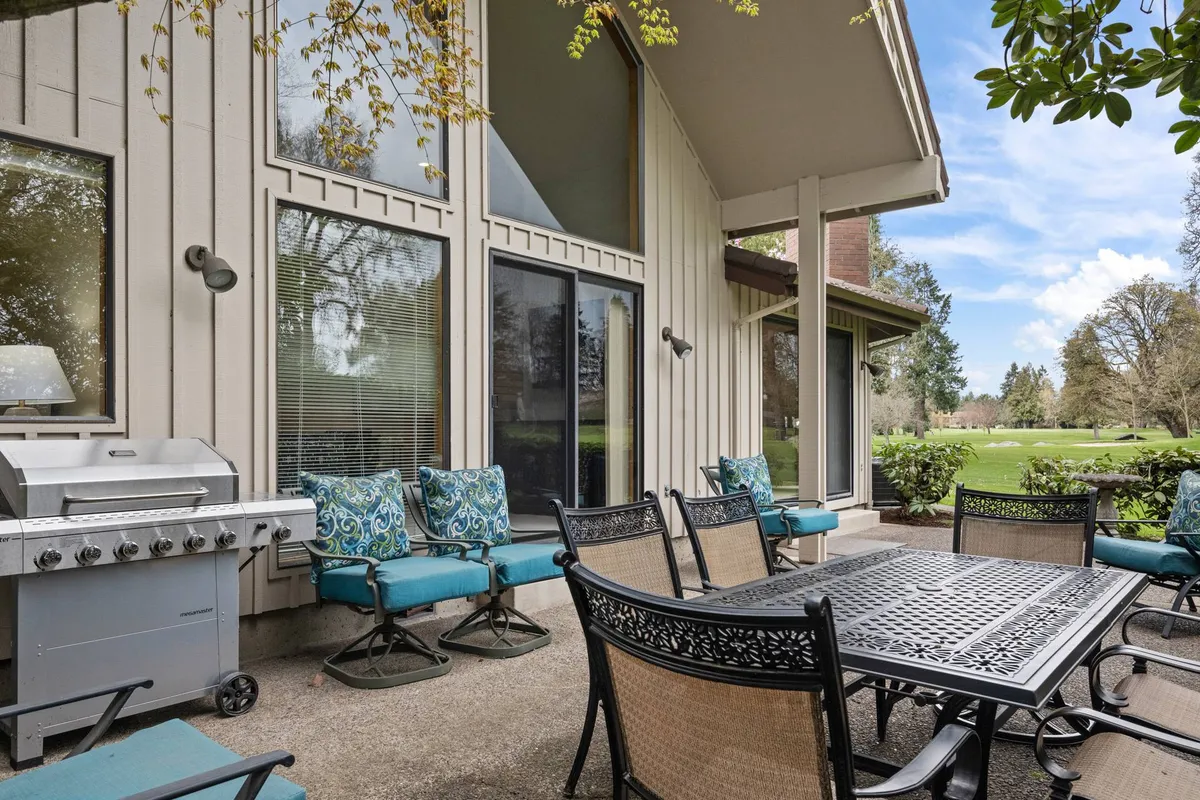 This exterior image highlights a spacious patio area featuring an outdoor dining table, a grill, and comfortable seating. Large windows provide a glimpse into the home's inviting interior, while the patio area is set up for gatherings, dining, and soaking in views.