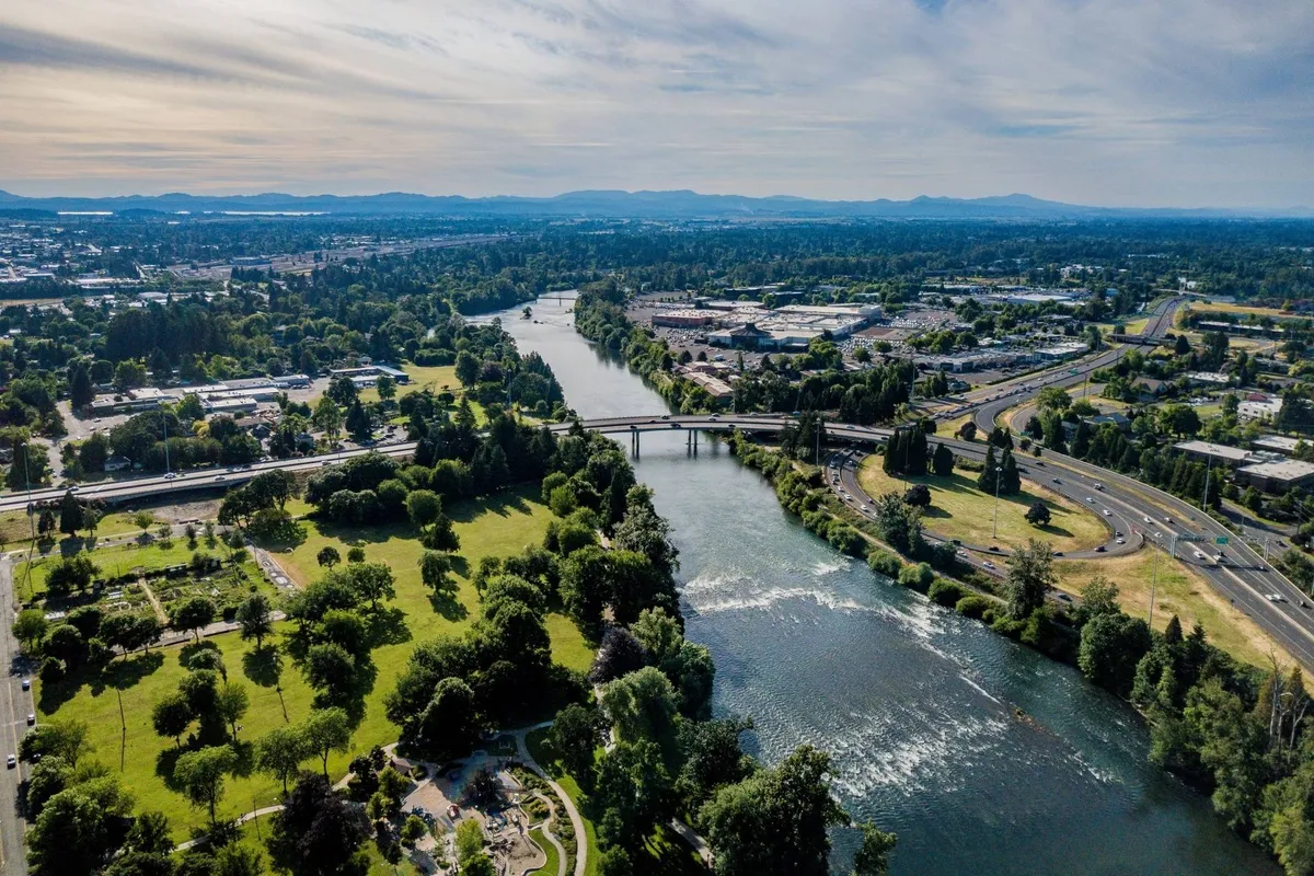 A sweeping view showcases a nearby river, a bridge, parkland, and the cityscape with mountains in the distance. The image is peaceful and expansive, suggesting recreational opportunities and scenic beauty in the surrounding area.