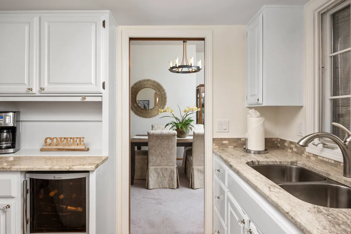 A bright and welcoming dining area featuring a coffee station, a stylish dining table, a decorative mirror, and a chandelier. The space is set up for both casual gatherings and special occasions, with ample seating and a layout that encourages conversation and group activities.